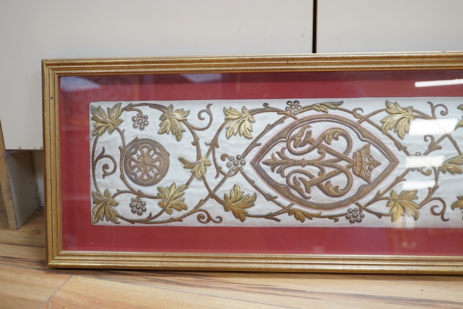 A framed Continental late 18th / 19th century heavily embroidered and deeply couched gold thread and white silk Orphrey panel, possibly part of a Chasuble or similar ecclesiastical garment, 18cm wide x 124cm long. Condit